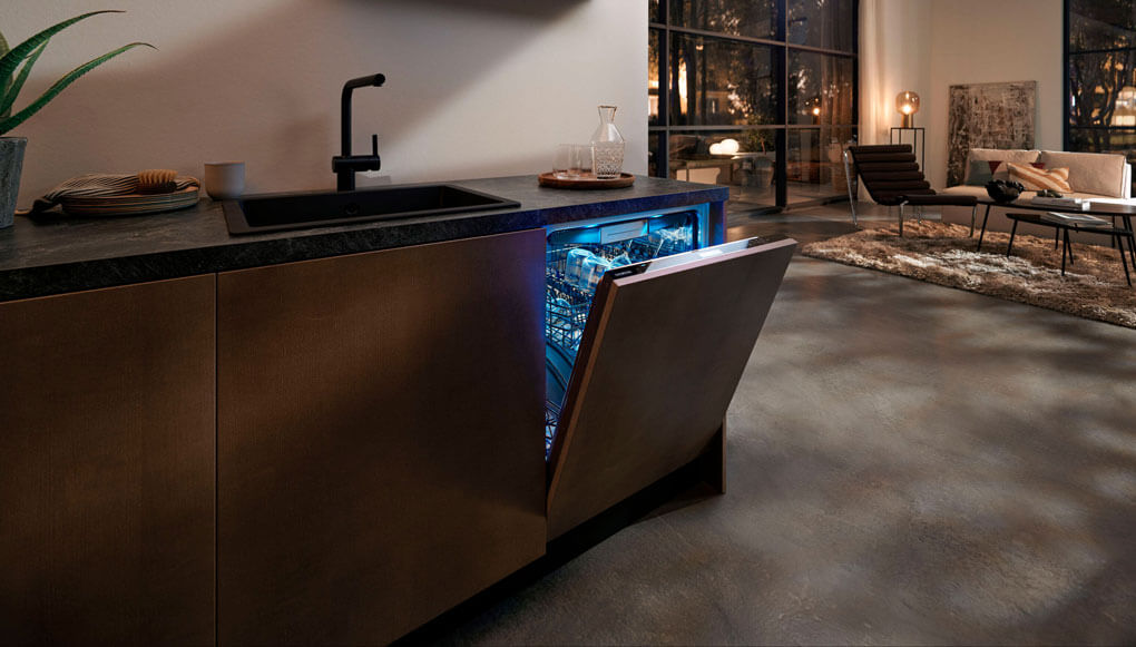 Een open keuken met een openstaande verlichte vaatwasser en een kraan in beeld.
